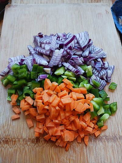 Ein Schneidbrett mit gewürfelten roten Zwiebeln, grüner Paprika und Möhre