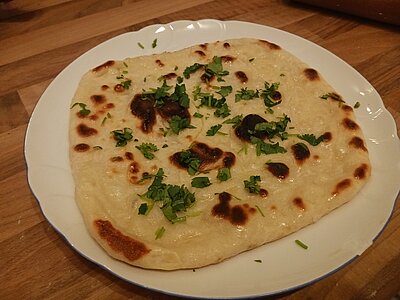 Ein flaches Naan auf einem Teller. Auf dem Brot ist Koriandergrün verteilt.