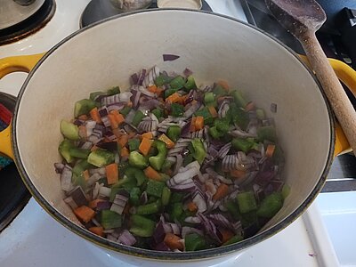 Ein Kochtopf in dem Zwiebeln, Paprika und Möhren angeschwitzt werden