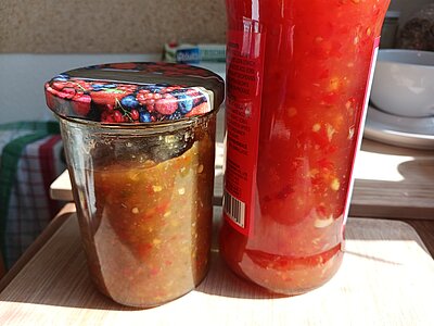 Ein Schraubglas gefüllt mit Chilie Soße neben einer Flasche mit Chilie Soße