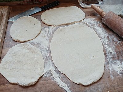 Vier ausgerollte Teigfladen auf einer Arbeitsoberfläche