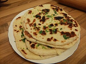Vier Naan auf einem Teller übereinander gestabelt. Sie sind mit Koriander garniert.